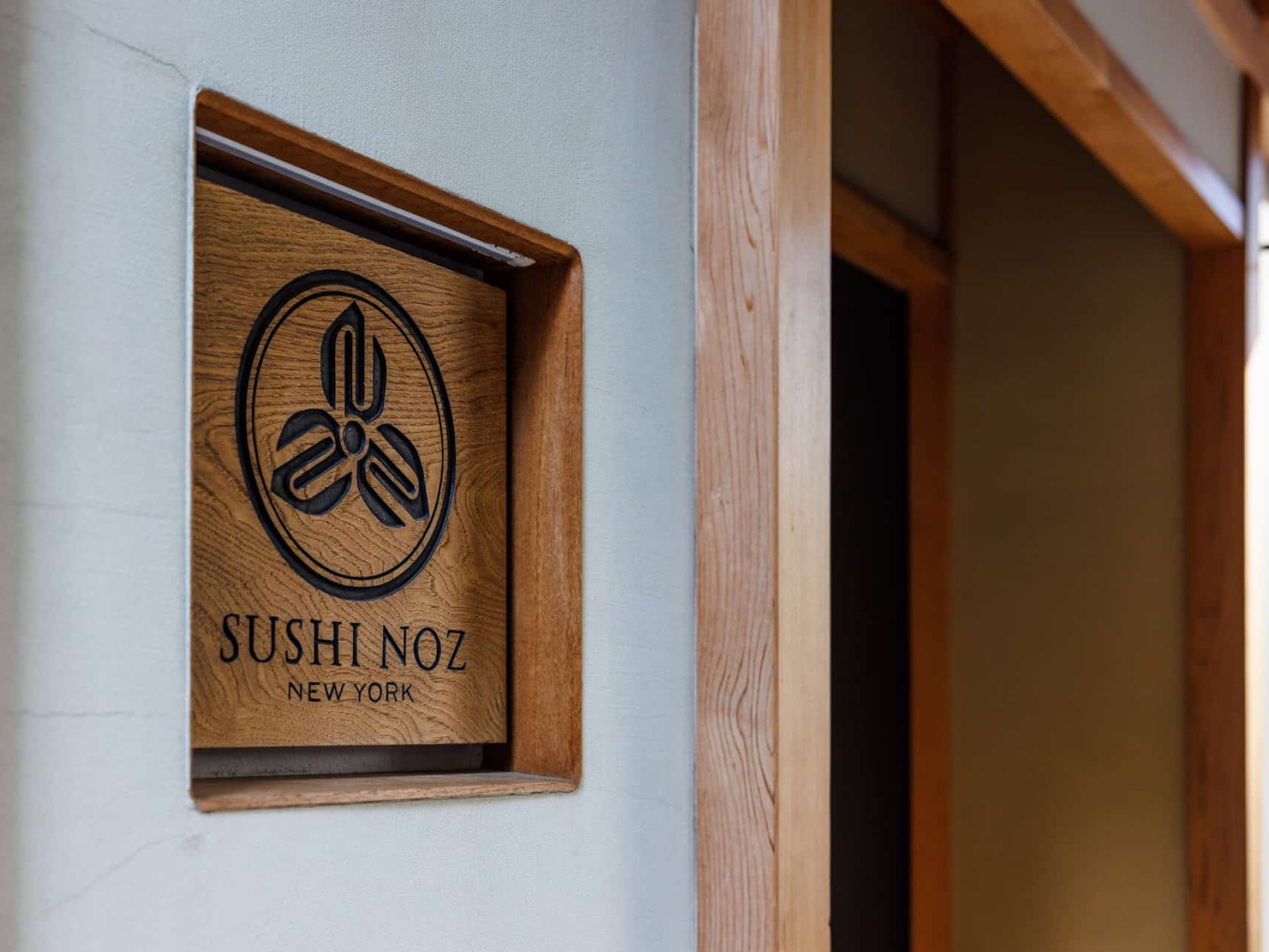Close up of a wood carved sign set into the wall at the entrance for Sushi Noz in New York City.